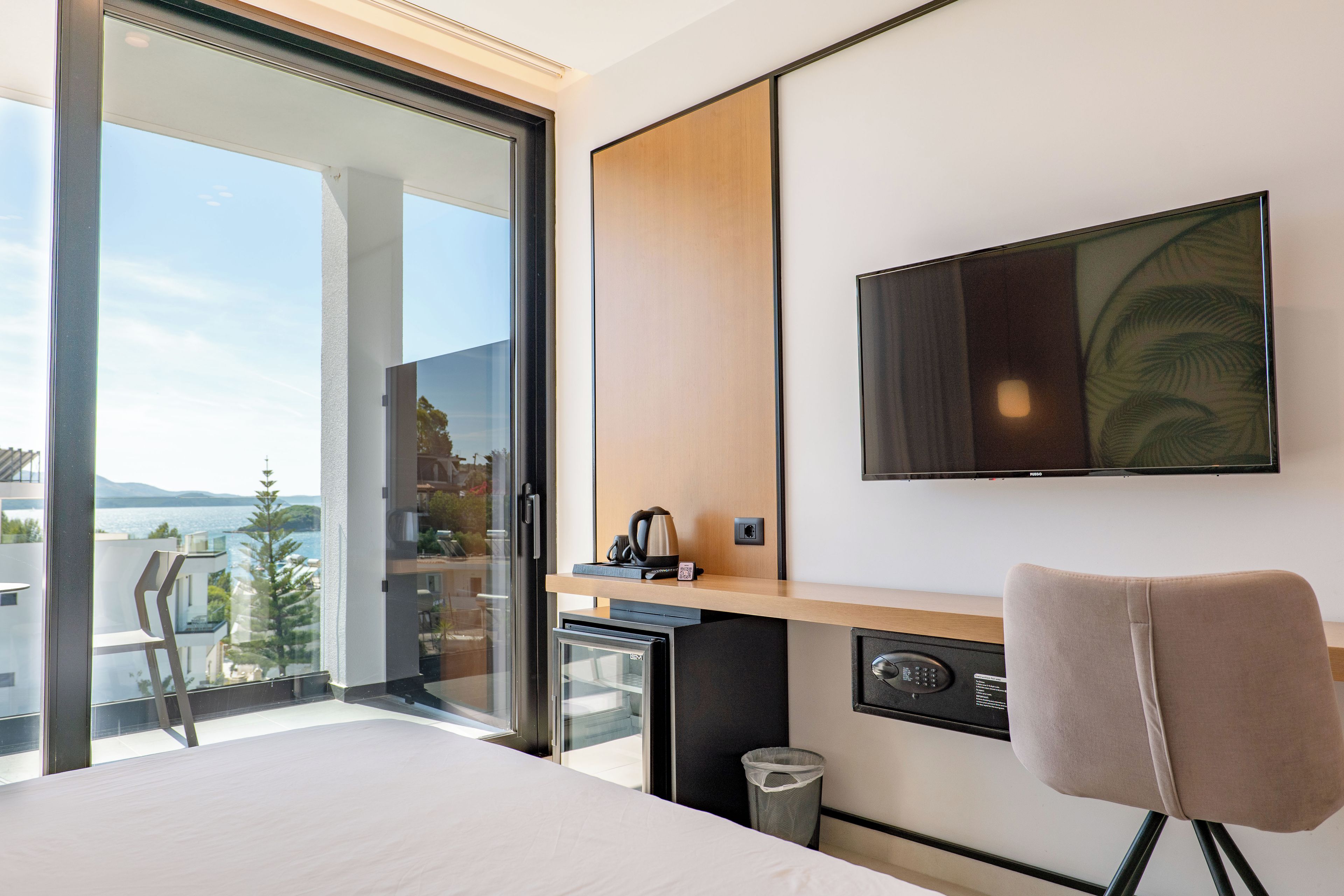 Une chambre d’hôtel avec un lit, un bureau, une chaise, une télévision et une vue sur la mer.