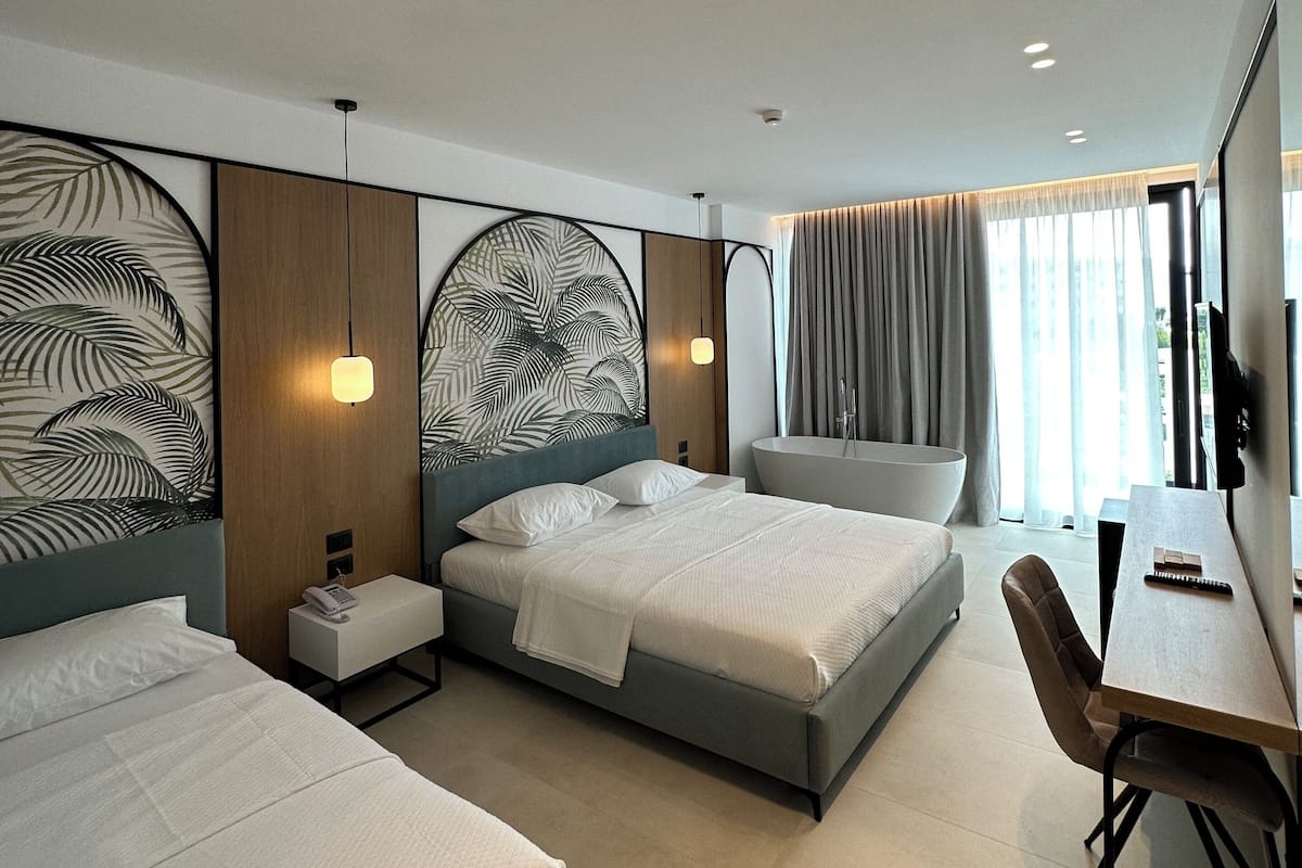 A modern hotel room with two beds, a desk, and a large window with curtains.
