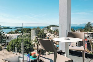 A balcony with a table and chairs overlooking a coastal view.