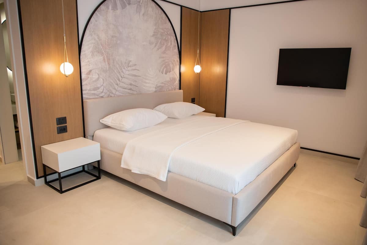 A modern bedroom with a large bed, bedside tables, a mounted TV, and a decorative wall panel.