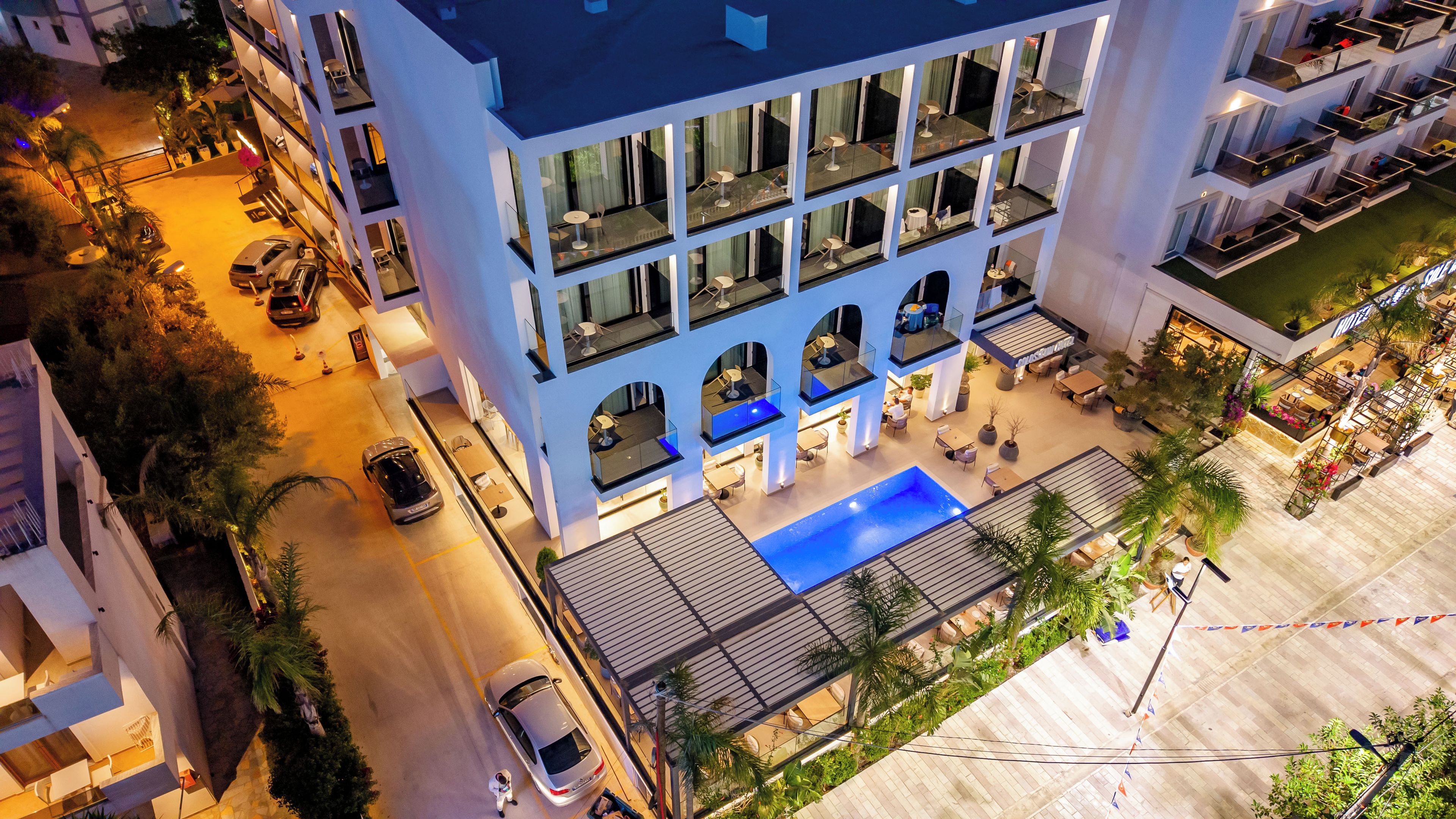 A multi-story hotel with a rooftop pool, outdoor seating, and a well-lit entrance.