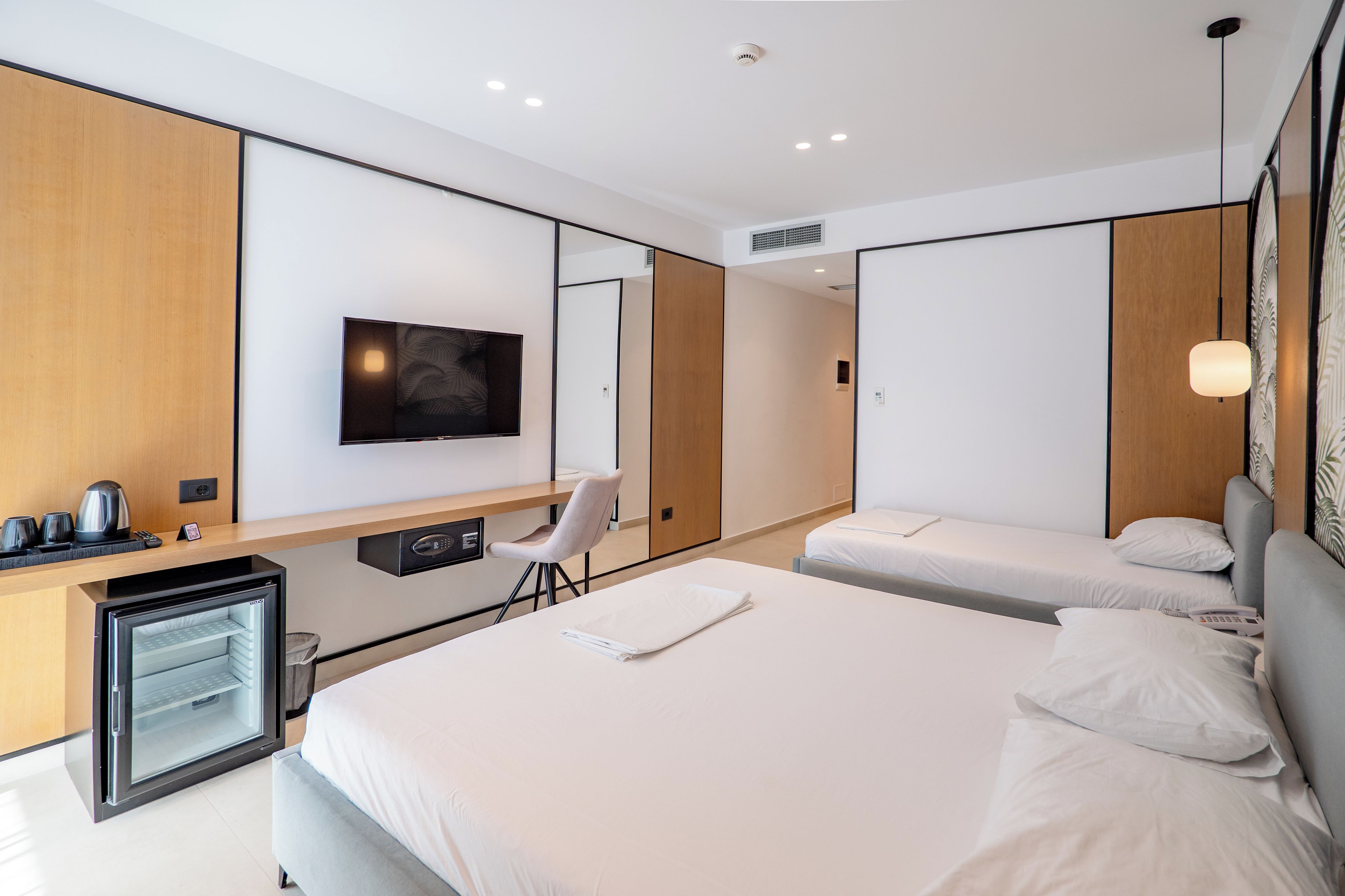 A modern hotel room with a large bed, a desk with a chair, a television, and a minibar.