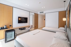 Una habitación de hotel moderna con una cama grande, un escritorio con una silla, televisión y minibar.