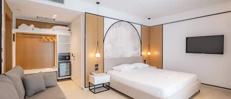 Una habitación de hotel moderna con cama, sofá, armario, minibar y televisión en la pared.