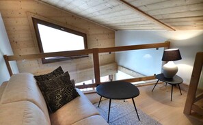 A modern living room with a wooden ceiling, a sofa with patterned cushions, a small round table, and a lamp.
