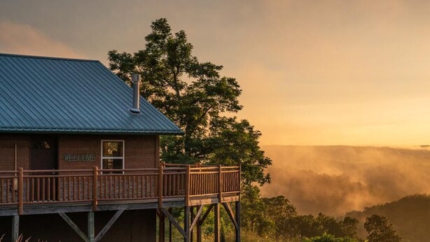 A wooden cabin with a metal roof, a deck, and a 'Welcome' sign. - Mountain Sunset Cabin w/ Hot Tub (Ponca)
