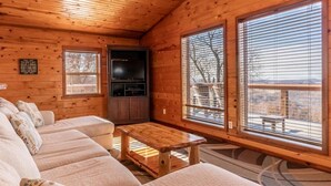 A cabin with a wooden interior, a sofa, a table, and a TV. - Mountain Sunset Cabin w/ Hot Tub (Ponca)