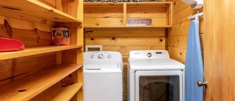 Uma lavanderia com duas máquinas de lavar brancas, uma prateleira com detergente Tide e uma placa com a inscrição 'LAUNDRY'.