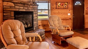 A cozy cabin interior with a stone fireplace, wooden walls, and two cushioned chairs. - Mountain Sunset Cabin w/ Hot Tub (Ponca)