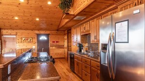 A kitchen with wooden cabinets, a stainless steel refrigerator, and a granite countertop island. - Mountain Sunset Cabin w/ Hot Tub (Ponca)