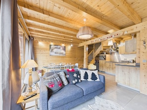 A cozy wooden cabin interior with a dining area, kitchenette, and a sofa with decorative pillows. - Les Gets - Premium Duplex Apartment in Village Center, 50m from Slopes (Les Gets)