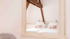 Een spiegel met houten lijst die een bed met witte lakens en bloemenkussens weerspiegelt.