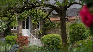 Een stenen gebouw met een witte deur, omgeven door weelderige begroeiing en een standbeeld.