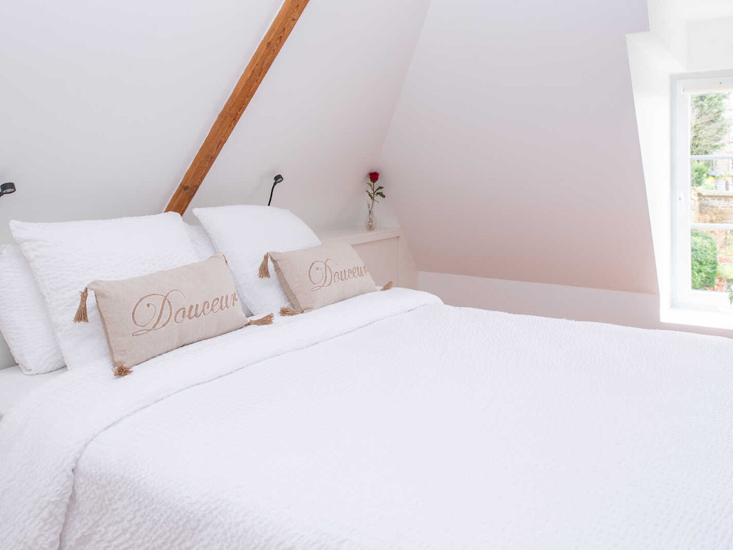 A bedroom with a sloped ceiling, a bed with white bedding, and two decorative pillows with the word "Douceur" on them.