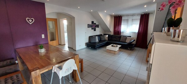 A living room with a black sofa, a wooden coffee table, and a dining area with a wooden table and white chairs.