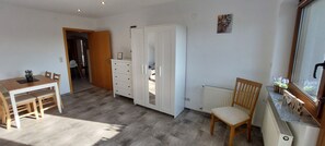 A room with a wooden dining table, a white wardrobe, a radiator, and a window with plants.