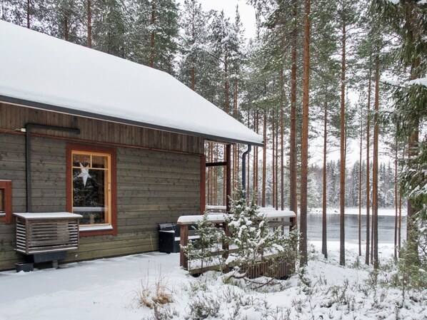 A cabin with a wooden exterior, a covered porch, and a view of a forested area.