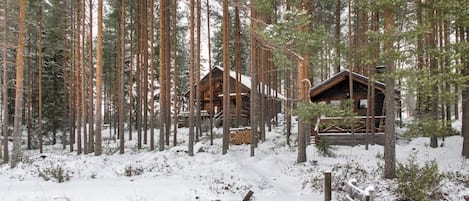 A cabin in a snowy forest with a wooden deck and a bench.