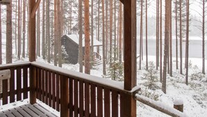 Puinen terassi, jolta avautuu näkymä lumiseen metsään ja siellä sijaitsevaan mökkiin.