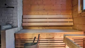 Una panca di legno con un secchio di metallo in una stanza con soffitto spiovente e parete in legno.