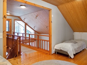 Een slaapkamer met een houten plafond, een bed, een raam en een trap.