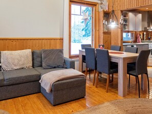 A cozy living room with a grey sofa, a small ottoman, and a dining area with a wooden table and chairs. - Lomahokkila by Interhome (Sotkamo)