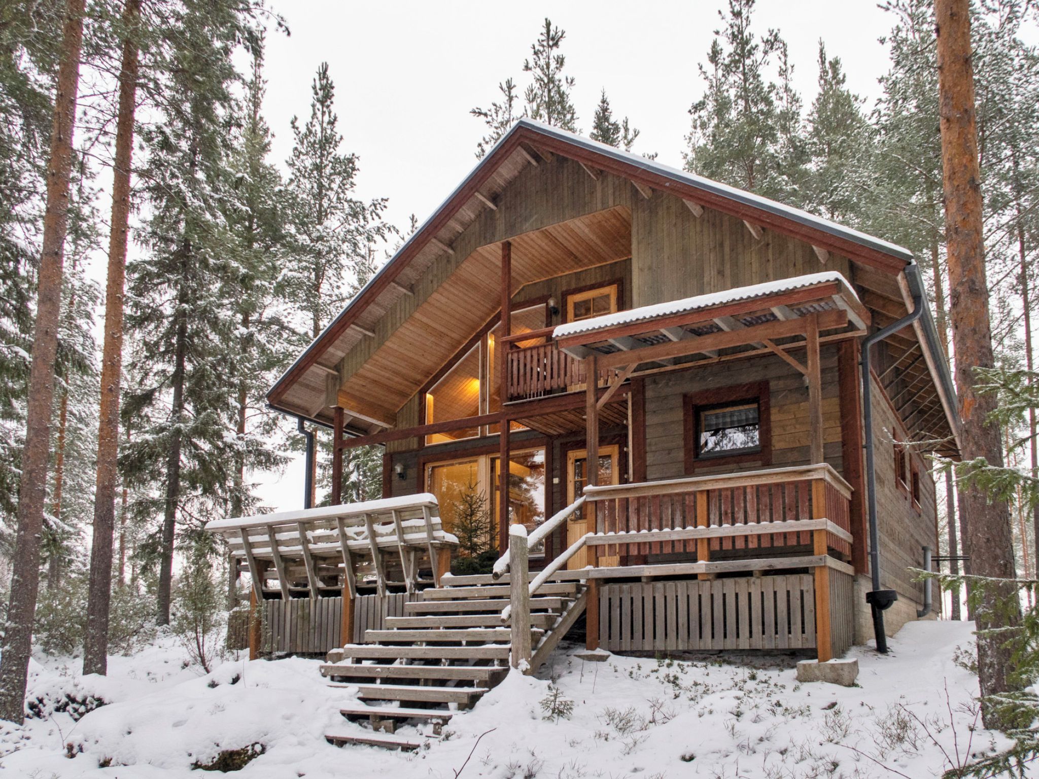 Una baita di legno con un balcone, immersa in alberi alti e coperta di neve.