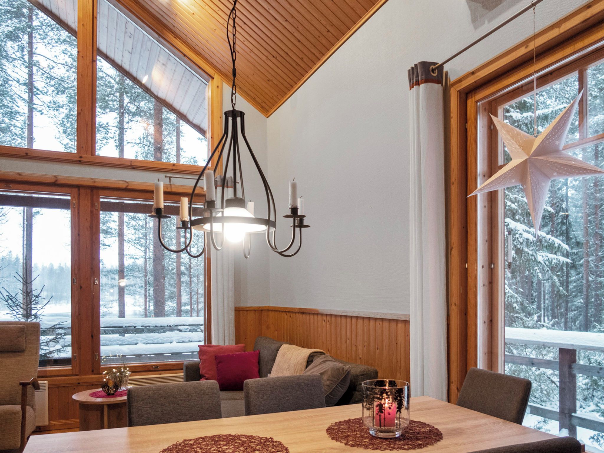 A cozy cabin interior with a wooden ceiling, large windows, a dining table, and a star decoration.