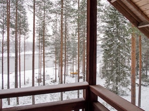 A view from a window with a wooden frame, overlooking a snowy forest with tall trees and a small cabin. - Lomahokkila by Interhome (Sotkamo)