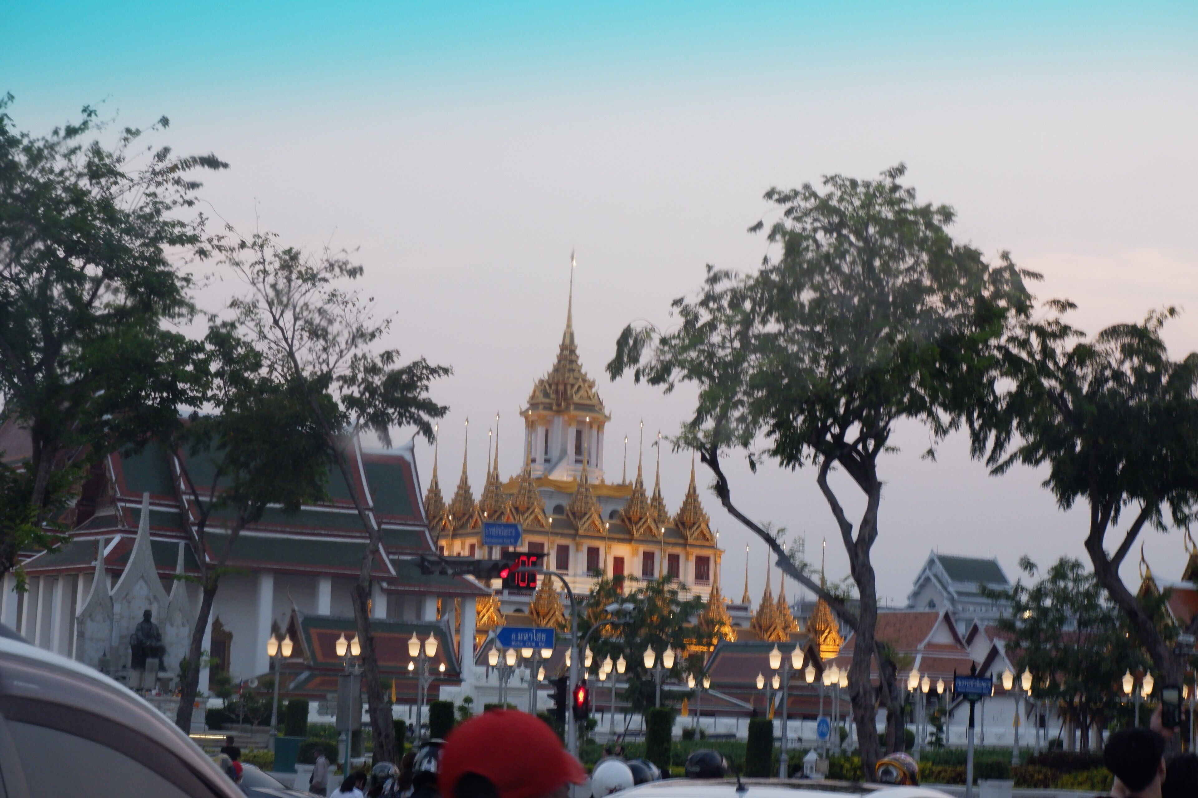 A traditional temple with a golden spire, surrounded by trees and street lamps.