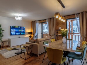 A modern living room with a sofa, dining table, chairs, and a TV mounted on the wall.
