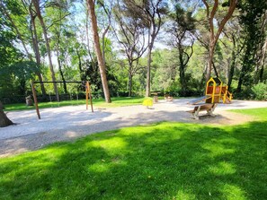 Explore a serene park setting with a playground featuring a swing set, slide, and climbing structure, surrounded by lush greenery and trees.