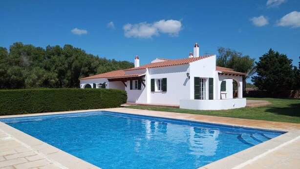 Una villa bianca con piscina, immersa nel verde e sotto un cielo sereno.