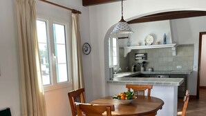 Un'area pranzo con un tavolo rotondo in legno, sei sedie e una ciotola di frutta.