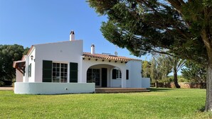 Un edificio bianco con persiane verdi, tetto in tegole e area d'ingresso pavimentata.