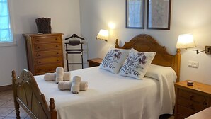 Un letto ben rifatto con testiera in legno, due lampade sui comodini, una cassettiera in legno e una finestra con vista sugli alberi.