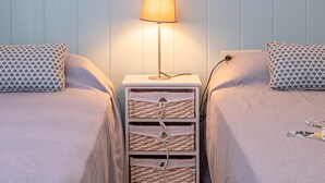 A twin room with two beds, a bedside table with a lamp, and a woven storage unit. - Modern Apartment Facing Sant Antoni Beach (San Antonio de Calonge)