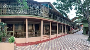Un edificio de dos plantas con balcón, columnas y un paseo empedrado.
