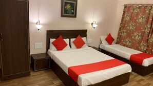 Habitación de hotel con dos camas, cada una con almohadas y cubrecama rojos. Se observa un armario de madera, una mesita de noche y un aplique de pared.