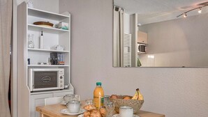 Ein Frühstückstisch mit Croissants, Saft und Obst, einer Mikrowelle und einem Regal mit Büchern und Küchenutensilien.