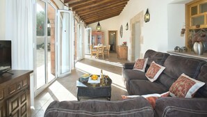 A spacious living area with a wooden ceiling, a sofa set, a television, and a dining area visible through glass doors. - Villa Armonia by Interhome (Jávea)
