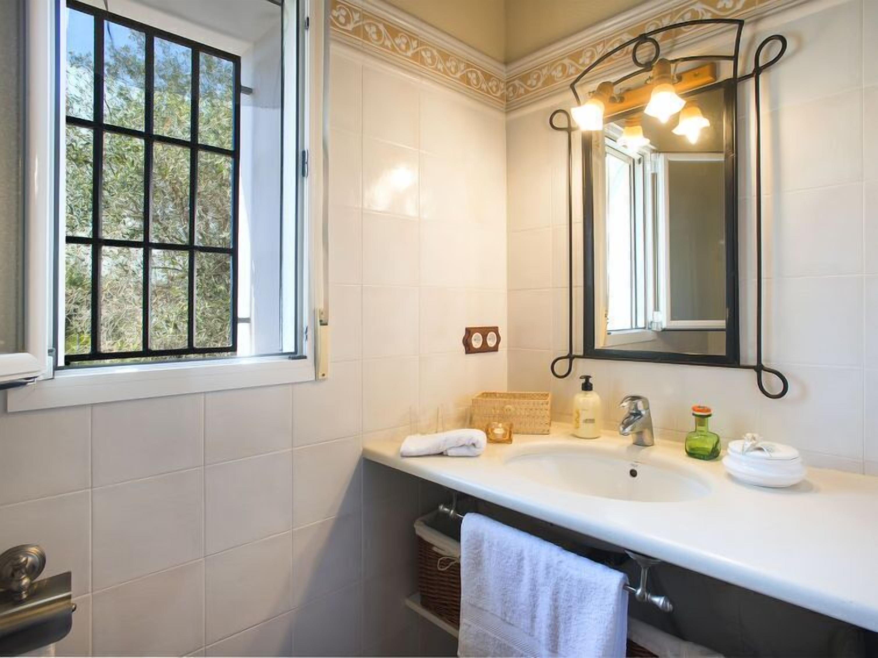 A bathroom with a white sink, a mirror, and a window.