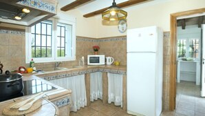A kitchen with a stove, microwave, and refrigerator. There is a window with curtains, a sink, and a ceiling fan. - Villa Armonia by Interhome (Jávea)