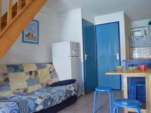 A compact living space with a sofa, a refrigerator, a blue door, and a small kitchen area with stools.