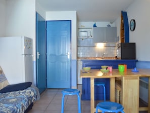 A compact kitchen with a blue door, a microwave, and a sink. There is a small table with stools and a bed with patterned bedding.