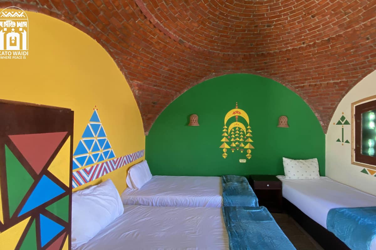 Een kamer met twee bedden, een bakstenen plafond en een groene wand met decoratief ontwerp.