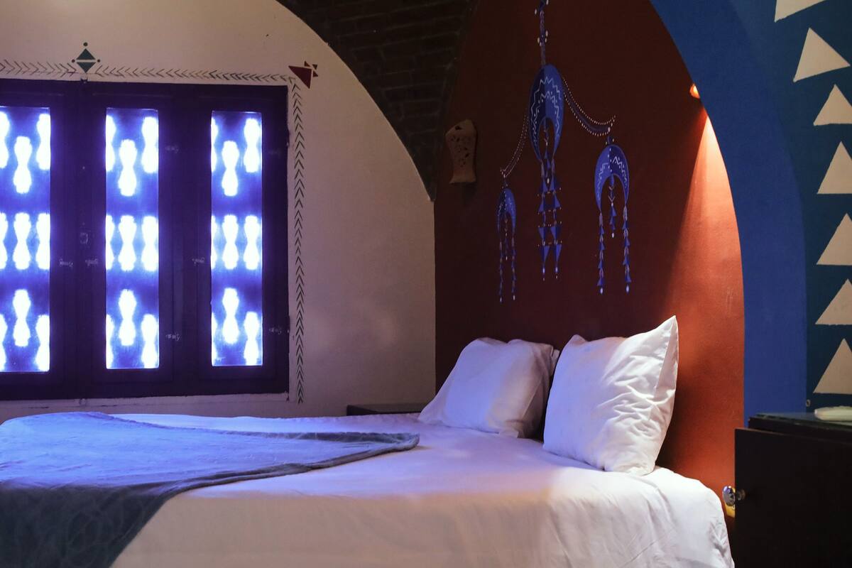 Een bed met witte lakens, een groot verlicht scherm en een muur met geometrische patronen.