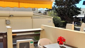 A terrace with a table and chairs, an air conditioning unit, and a yellow awning. - Cozy Air-Conditioned Studio, Terrace, WiFi, Parking - South-Facing, 2 Guests (Cap d'Agde naturisme)