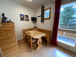 Una stanza con un tavolo di legno e panche, un televisore a parete e una finestra vista alberi.