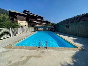 Una piscina rettangolare con un trampolino al centro, circondata da un solarium in cemento.